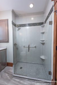 glass walk in shower featuring grab bars, soap shelves, shaving shelves and more in remodeled bathroom